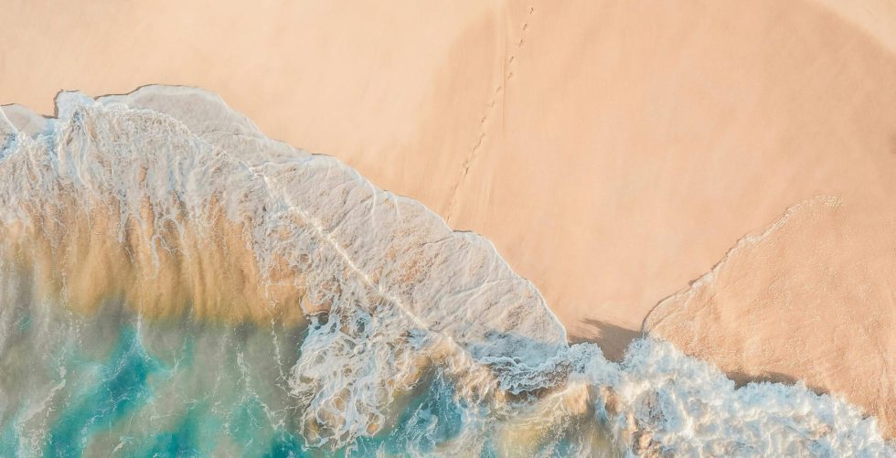 Drone view of anonymous person walking along sandy beach of turquoise sea in sunny day